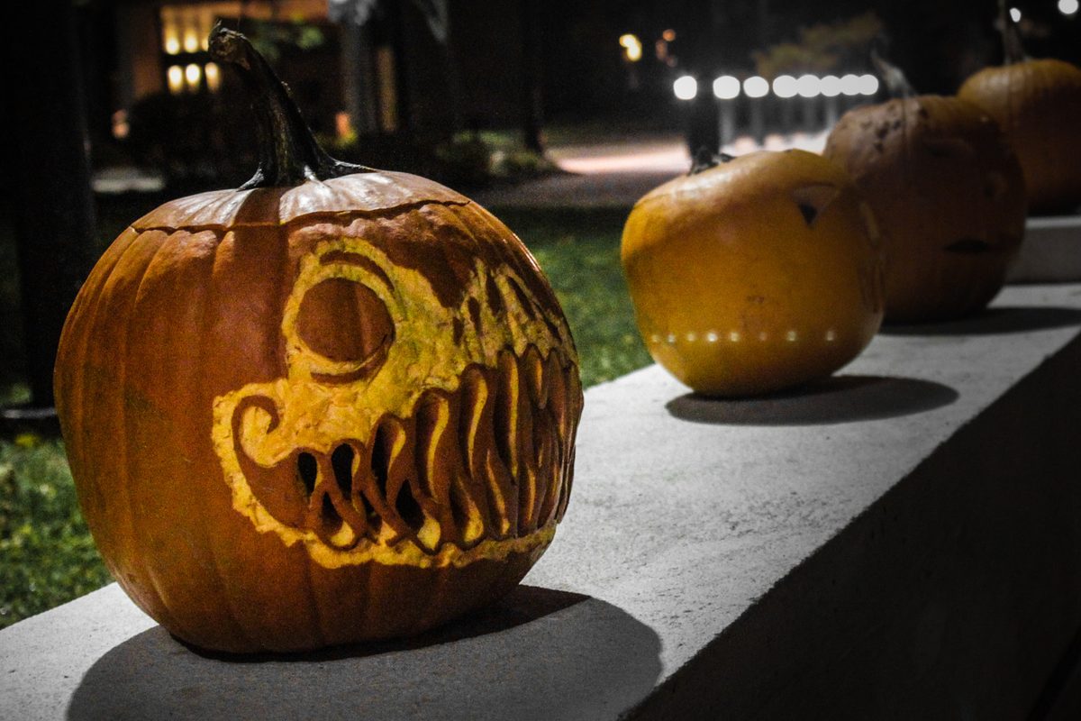 Carabasses d'Halloween tallades sobre un mur de nit; en primer pla, una amb cara de monstre i dents esmolades