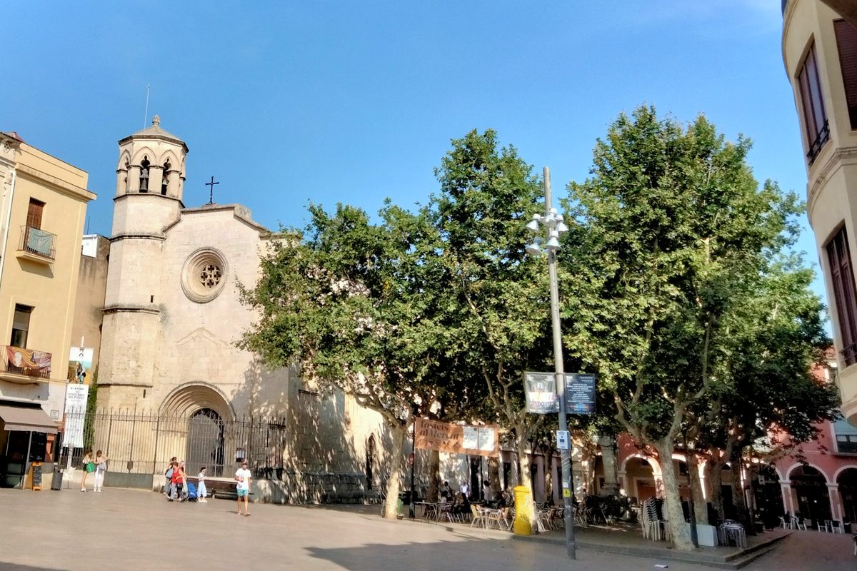 Església de Sant Joan i arbres de la plaça de la Vila de Vilafranca del Penedès, vistos des d'un arc